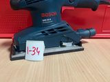 un gros plan d'une ponceuse Bosch posée sur une table, à côté d'une boîte rouge