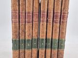 six old books are lined up in a row on a white surface