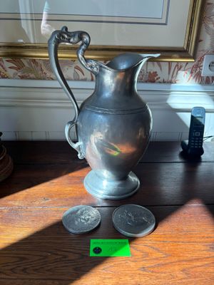 a silver pitcher sitting on a wooden table next to some coins