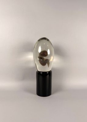 une petite boule de verre avec un socle noir posée sur une surface blanche