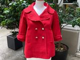 red wool coat on a mannequin stand in front of a potted plant