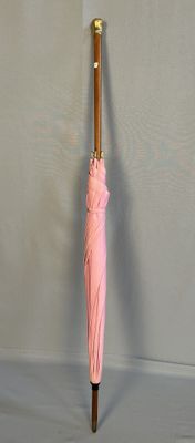un parapluie rose avec un manche en bois accroché au mur