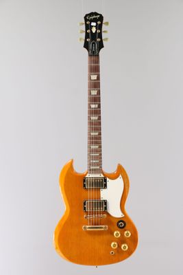 an orange electric guitar hanging from a string on a white wall