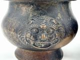 a metal vase with a face on it on a white surface