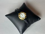 un petit oreiller noir sur lequel repose une montre en or
