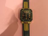 une image représentant une montre-bracelet noire et dorée posée sur un fond rose