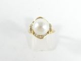 une photo d'une bague en perle blanche et diamants posée sur une surface blanche