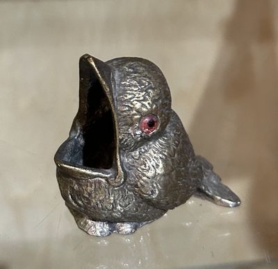 figurine en argent représentant un oiseau aux yeux rouges, posé sur une table en verre