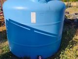 un grand réservoir d'eau bleu posé dans l'herbe, près d'une clôture