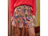 a woman in a red sweater and floral skirt standing in front of a mirror