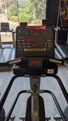 a tread machine in the gym with a view of the trees outside