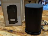 a black speaker sitting on top of a wooden table next to a box