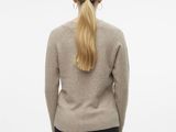 a woman in a beige sweater and black pants stands facing away from the camera