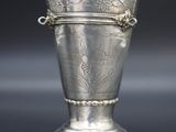 un vase ancien en argent posé sur un socle, sur une surface noire