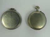 two silver pocket watches sitting side by side on a white surface