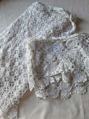 une veste blanche au crochet posée sur un lit, à côté d'un oreiller