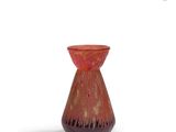 un vase rouge posé sur une surface blanche