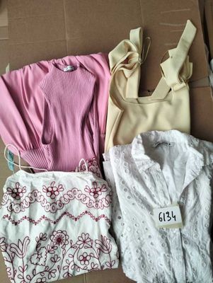 Trois vêtements pour femmes sont posés sur un carton posé par terre.