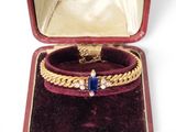 a gold bracelet with a blue stone in a red case