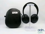 deux casques audio noirs posés sur un support blanc à côté d'un étui noir