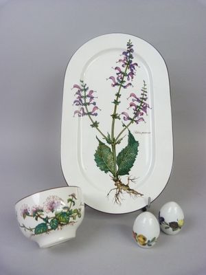 a white plate with purple flowers on it next to a cup and saucer