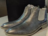 des bottines en cuir argenté posées sur une table blanche, avec une boîte noire en arrière-plan