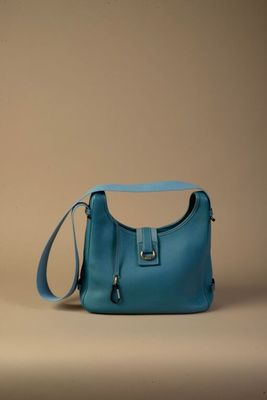 sac à main en cuir bleu avec une bandoulière, sur fond beige