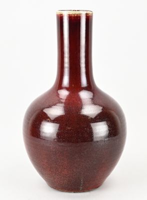 un vase rouge posé sur une surface blanche