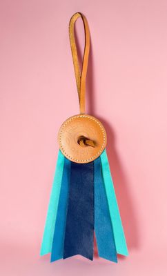 a blue and green ribbon with a wooden button on a pink background