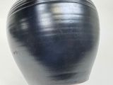 a black vase on a white table with a white background