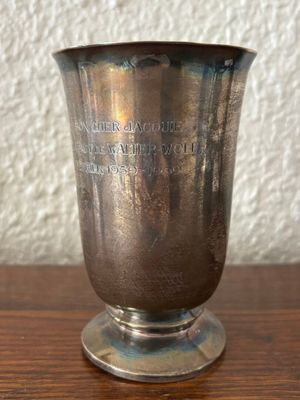 a silver cup on a wooden table with a white wall in the background