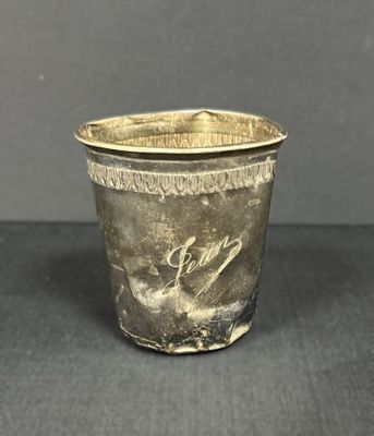 une tasse en métal argenté ornée d'un oiseau, posée sur une table