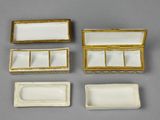 three small white and gold boxes with lids on a gray surface