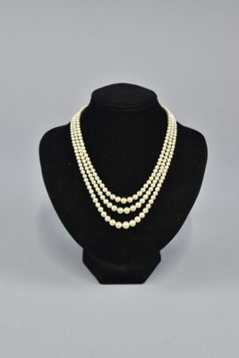 a white pearl necklace with three strands of pearls on a black mannequin