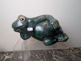 une statue de grenouille verte posée sur un socle transparent, sur un sol en marbre