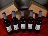 six bottles of red wine sitting next to a wooden box on a red cloth