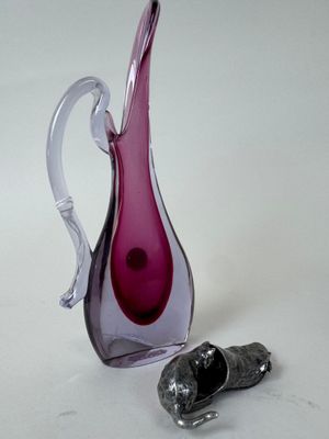 un vase en verre violet et un objet en argent posés sur une surface blanche