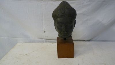 une photo représentant une statue représentant une tête posée sur un socle en bois