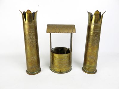 trois vases en laiton avec leurs couvercles et un socle, posés sur une surface blanche