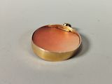 a close up of a gold and pink pendant on a white surface