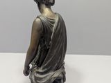 bronze statue of a woman sitting on a stool with her hands on her knees