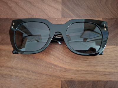 des lunettes de soleil noires posées sur une table en bois, à côté d'une paire de lunettes noires
