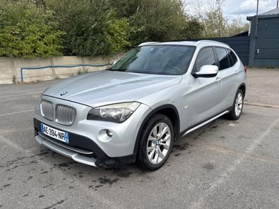 Le SUV BMW argenté est garé sur un parking devant un immeuble.