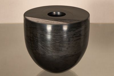 un vase noir posé sur une table, avec un mur blanc en arrière-plan