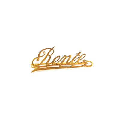 un gros plan d'une broche plaquée or sur laquelle est inscrit le mot « Renée »
