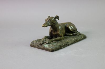 statue en bronze représentant un chien allongé sur un rocher, posée sur un socle blanc