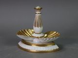 a white and gold vase on a stand on a table