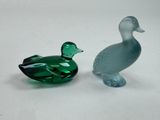 two glass ducks sitting next to each other on a white surface