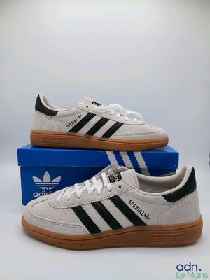 une paire de baskets Adidas blanches et noires posées sur une boîte bleue