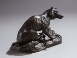 statue en bronze représentant un chien assis sur un rocher, un oiseau dans la gueule